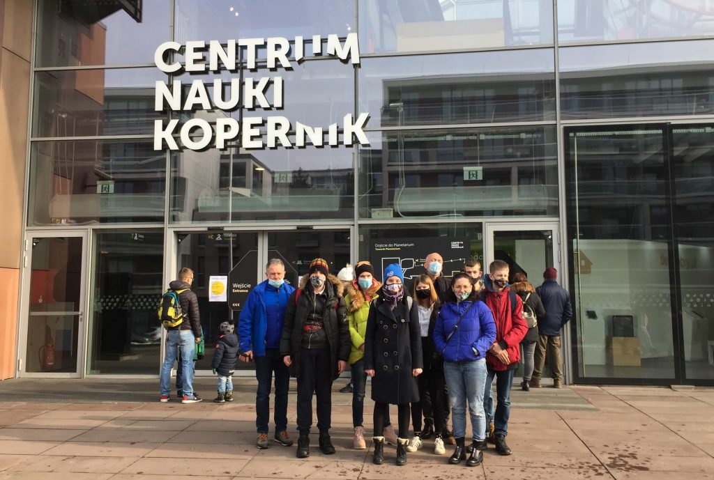 Grupa młodzieży pozuje do zdjęcia na tle budynku Centrum Nauki Kopernik w Warszawie.
