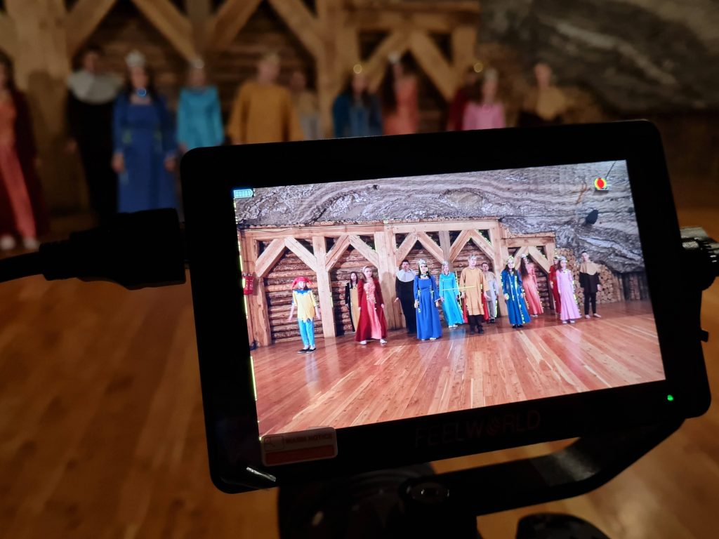 Na wyświetlaczu tableta widać ustaeioną w rzędzie młodzież przebraną w średniowieczne stroje.