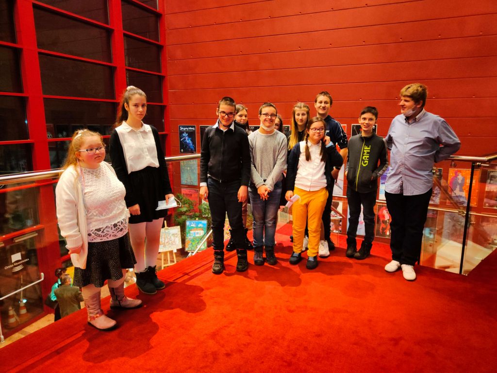 Grupa młodzieży pozuje do zdjęcia na tle czerwonej ściany.