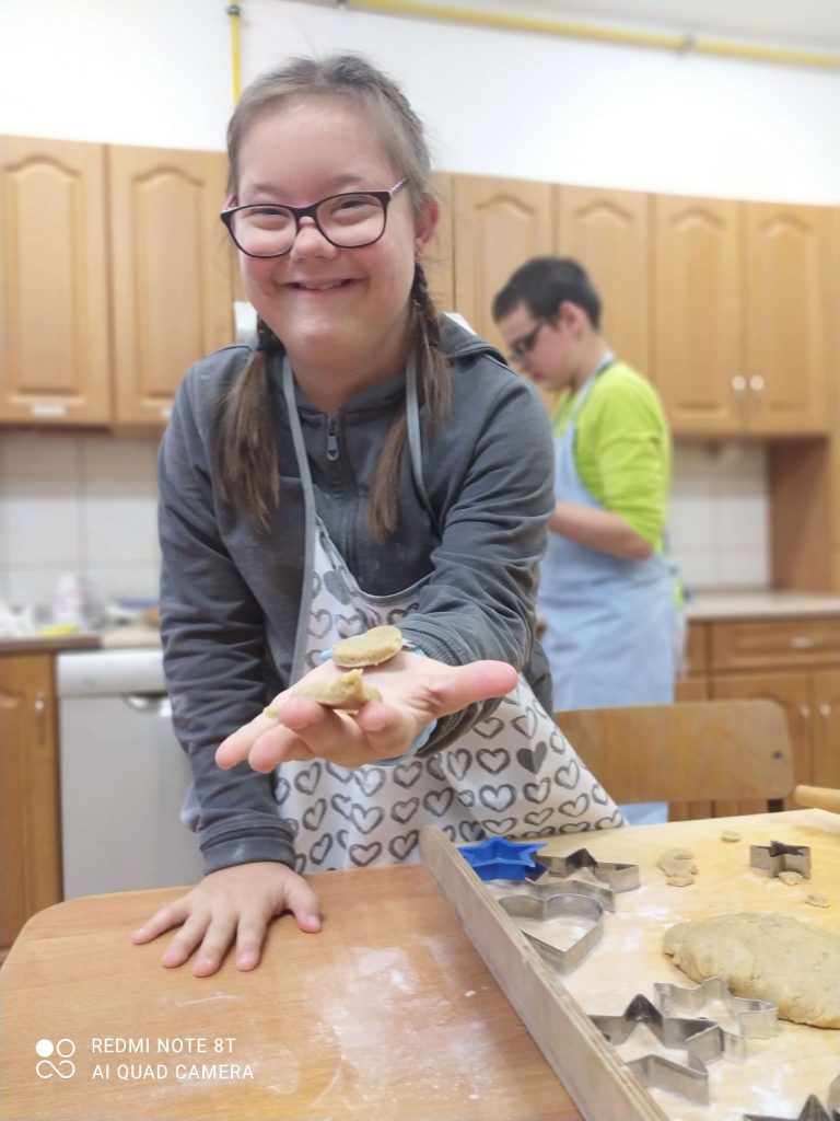 Uśmiechnięta dziewczynka w okularach wyciąga dłoń, na której jest ciasteczko piernikowe.