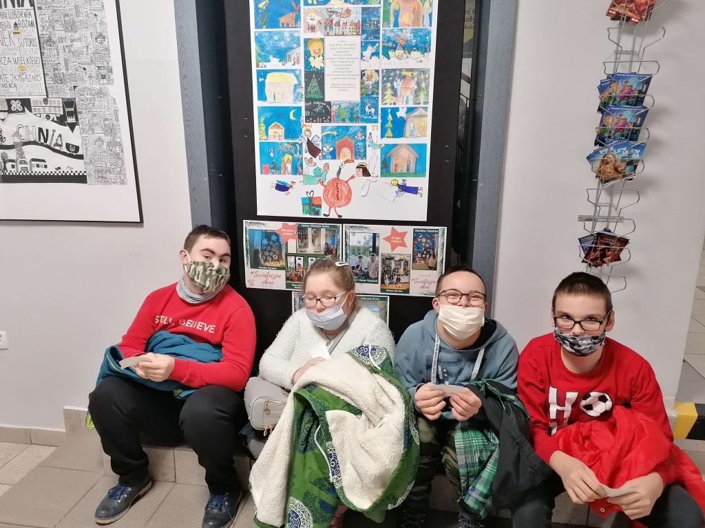 Czworo uczniów siedzi na schodku. Za nimi widoczne są plakaty filmowe.