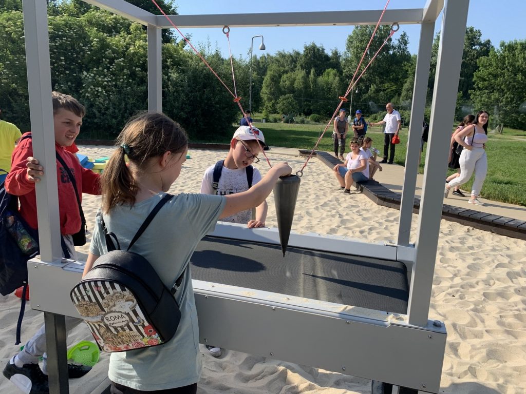 Młodzież w Ogrodzie Doświadczeń w Krakowie. Dziewczynka z plecakiem wykonuje rysunek piaskiem.