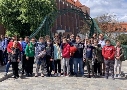 Grupa młodzieży pozuje w szeregu do zdjęcia na tle zabudowań Ostrowa Tumskiego we Wrocławiu.