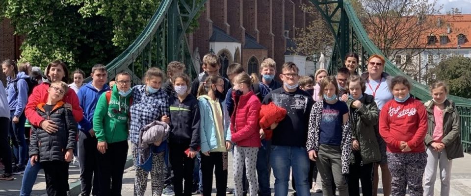 Grupa młodzieży pozuje w szeregu do zdjęcia na tle zabudowań Ostrowa Tumskiego we Wrocławiu.