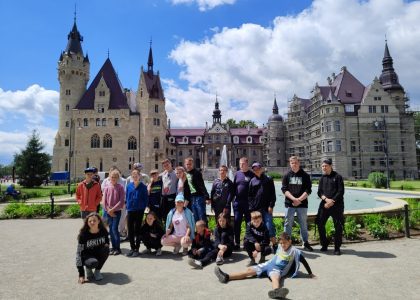 Grupa młodzieży pozuje do zdjęcia na tle Zamku w Mosznej.