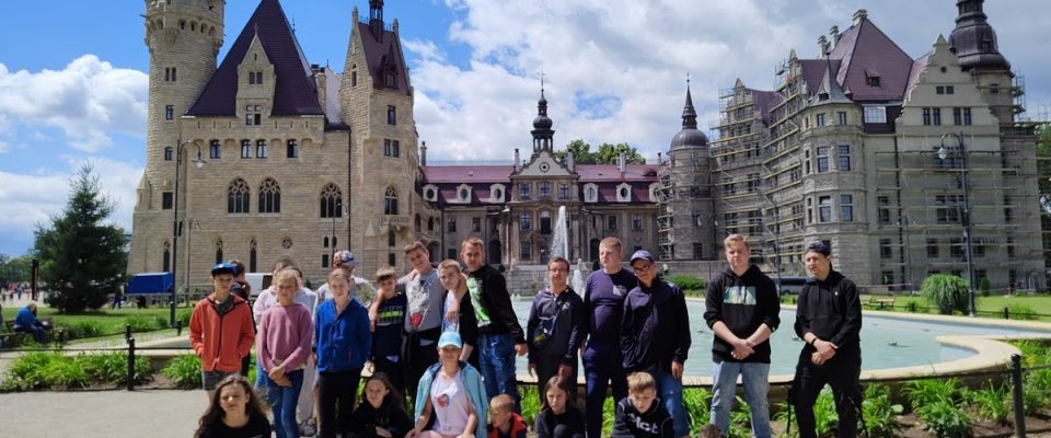 Grupa młodzieży pozuje do zdjęcia na tle Zamku w Mosznej.