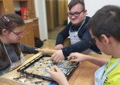 Trzech chłopców siedzi przy stole i układa pierniki na blaszce do pieczenia.