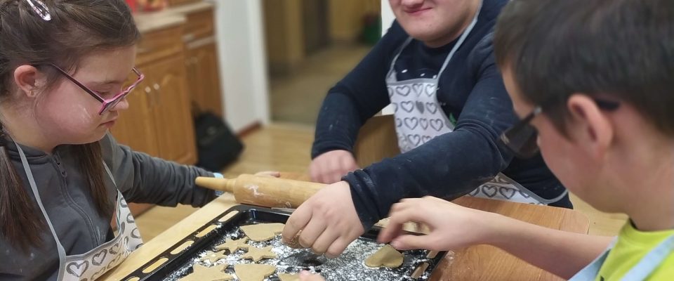 Trzech chłopców siedzi przy stole i układa pierniki na blaszce do pieczenia.