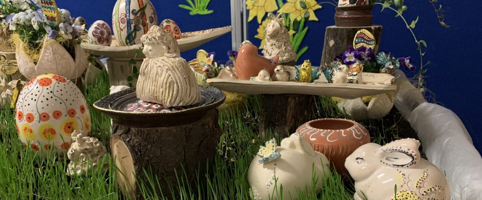 Ozdoby wielkanocne z ceramiki ustawione na stole w trawniku z młodego owsa.