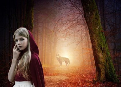 mała dziewczynka w czerwonym kapturze, w tle stoi wilk.