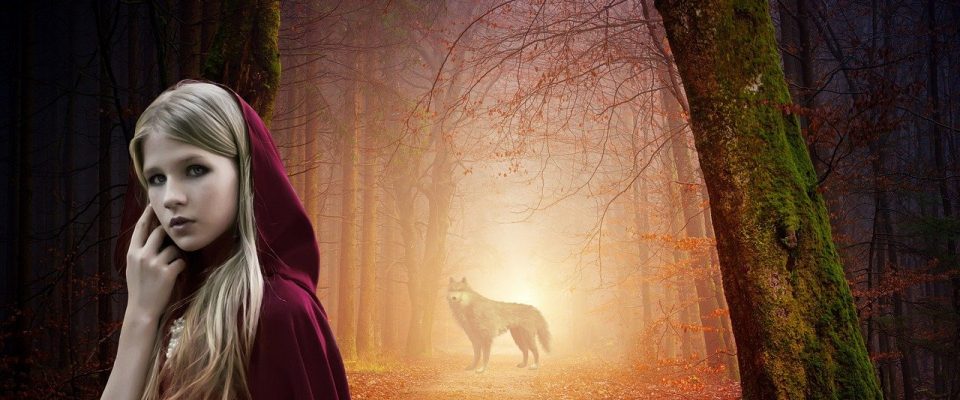mała dziewczynka w czerwonym kapturze, w tle stoi wilk.