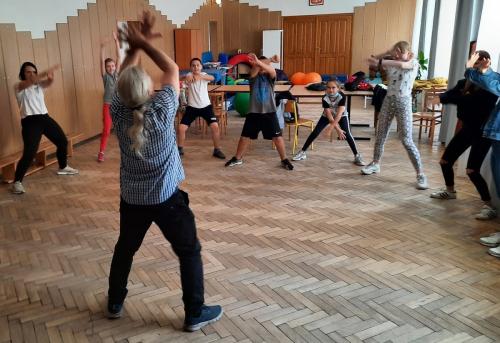 Grupa dzieci oraz mężczyzna unoszą do góry ręce.