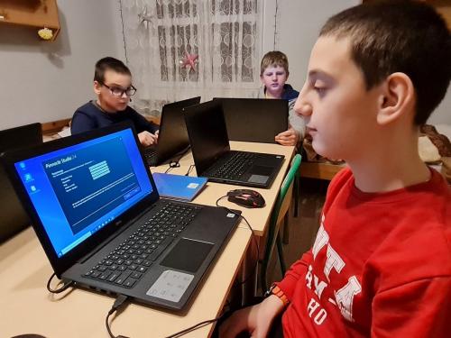 Trzech chłopców siedzi przy stoliku i patrzy na ekrany laptopów.