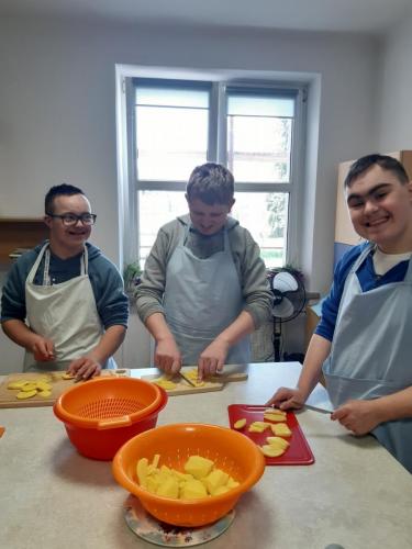 Trzech chłopców w fartuszkach kuchennych kroi ziemniaki.