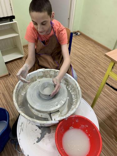 Chłopiec formuje rzeźbę na kołem garncarskim.