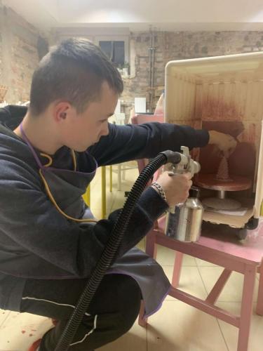 Chłopiec maluje pistoletem ceramiczną figurkę.