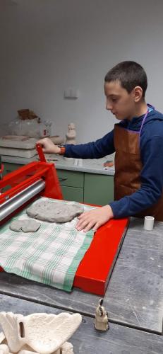 Chłopiec rozwałkowuje glinę przy użyciu specjalnej prasy.