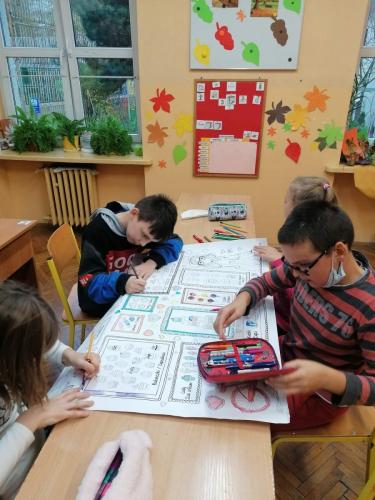 Czworo dzieci siedzi przy stoliku i wspólnie maluje na dużej kartce.