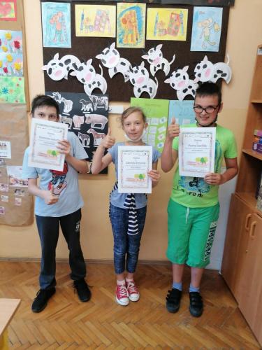 Troje dzieci stoi i prezentuje papierowe dyplomy.