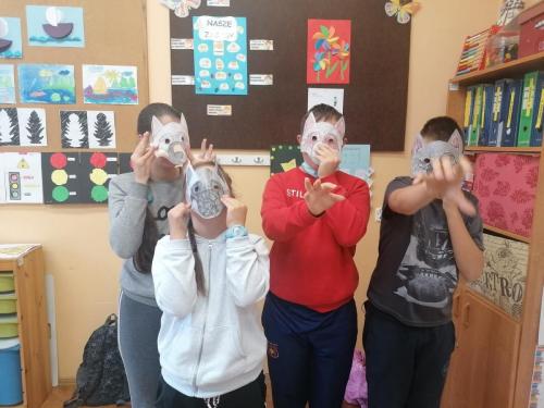 Czworo dzieci stoi trzymając przy twarzach maski zwierząt.