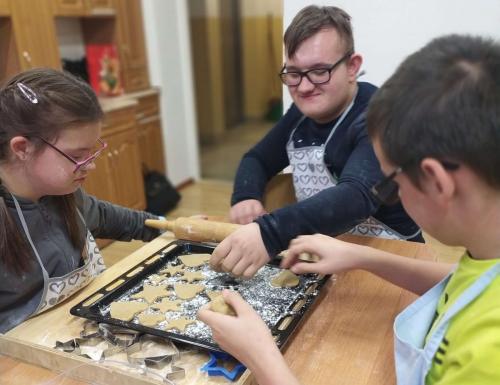 Trzech chłopców siedzi przy stole i układa pierniki na blaszce do pieczenia.