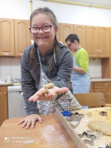 Uśmiechnięta dziewczynka w okularach wyciąga dłoń, na której jest ciasteczko piernikowe.