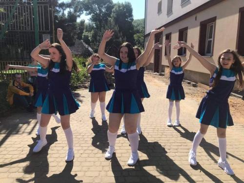 Grupa dziewcząt w strojach czirliderek stoi z uniesionymi rękami.