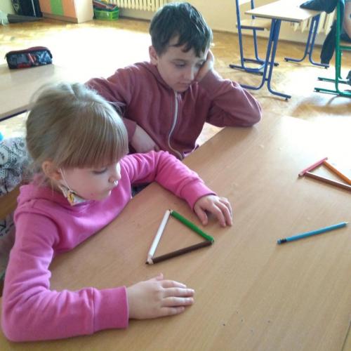 Dwoje dzieci w różowych bluzach siedzi przy stoliku i układa kształty z kredek.